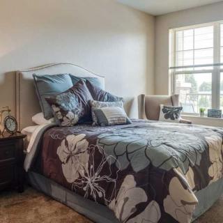 A cozy bedroom with a floral comforter and plush pillows, illuminated by natural light from a large window.