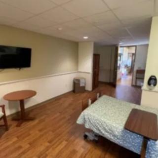 A hospital room featuring a bed, television, table, and chair.