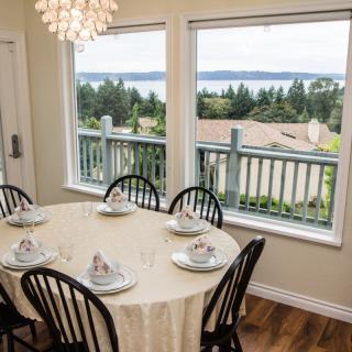A dining room with a table set for six, overlooking a scenic view through large windows.