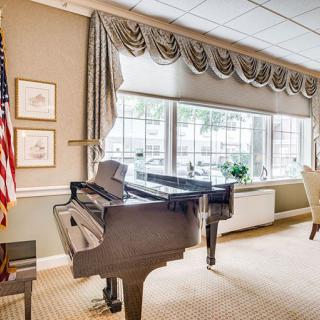 A cozy room featuring a grand piano and large windows with elegant drapes, accompanied by an American flag.