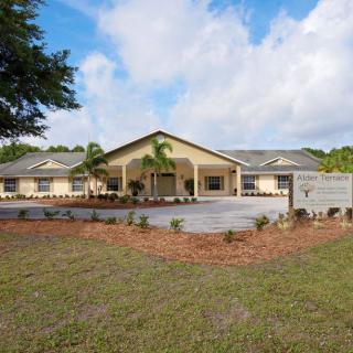 A single-story building with a driveway and landscaped garden under a cloudy sky.