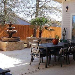 A cozy backyard patio featuring a dining table, chairs, and a beautiful fountain.