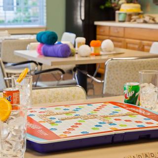 A cozy kitchen setting featuring a colorful board game on the table, with yarn and beverages in the background.