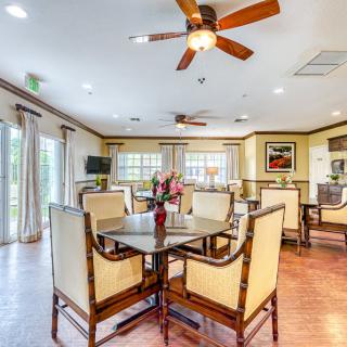 A well-lit dining area with elegant furniture and a ceiling fan, featuring large windows and wooden flooring.