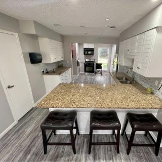 A modern kitchen interior featuring a granite countertop and bar stools, with an open space layout.