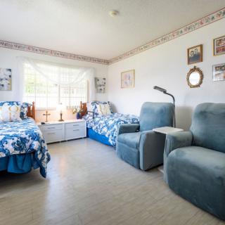 A cozy bedroom with twin beds, armchairs, and a bright window.