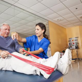 A healthcare professional assists an elderly man with physical therapy exercises using resistance bands.