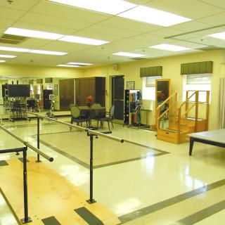 A physical therapy rehabilitation room equipped with parallel bars and various exercise equipment.