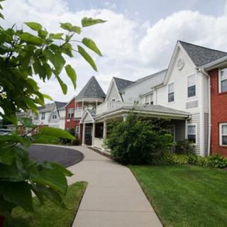 A picturesque residential building with a well-maintained landscape and a clear sidewalk, set against a cloudy sky.