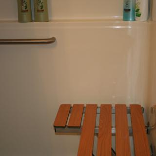 An accessible shower with a wooden bench and grab bar.