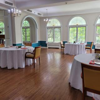A spacious and elegantly decorated event space featuring round tables, colorful chairs, and ample natural light.