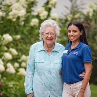 An elderly woman and a young woman smiling in a garden full of flowers.