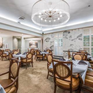 An elegant dining area with neatly arranged tables and chairs under a chandelier.
