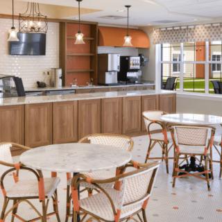 A modern cafe interior featuring round tables and chairs, with a counter area and pendant lighting.