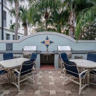 Outdoor patio with grill and seating area surrounded by palm trees.