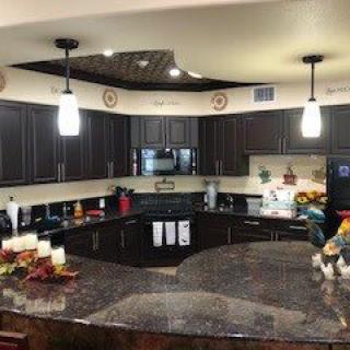 A modern kitchen with dark cabinets and granite countertops, featuring pendant lighting and decorative elements.