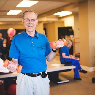 An elderly man exercising with dumbbells in a gym setting.