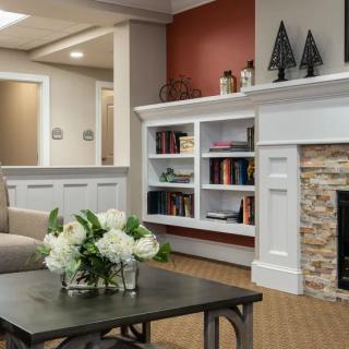A cozy living room with a modern fireplace and a well-organized bookshelf, adorned with decorative items and fresh flowers.