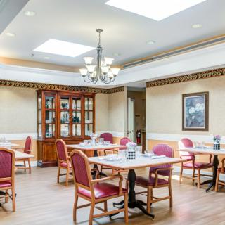 A well-lit dining room with elegant tables and chairs, featuring a chandelier and a wooden cabinet.