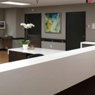 A modern reception area with a white desk, decorative flowers, and abstract artwork on the wall.