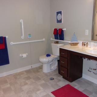 An accessible bathroom with grab bars, a toilet, sink, and red and blue accents.