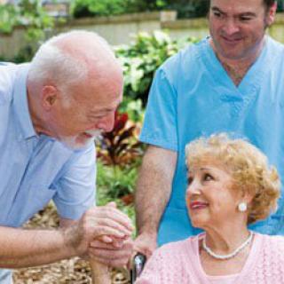 A caregiver assisting an elderly woman in a wheelchair, with another person engaging with them outdoors.