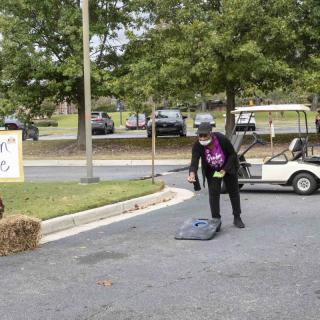 A person in a Halloween costume stands on the street near a golf cart, surrounded by autumn decorations.