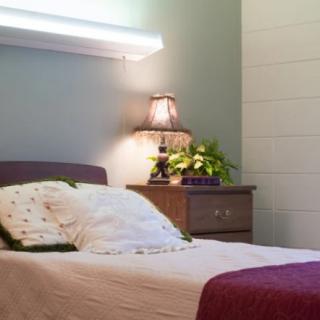 A cozy bedroom featuring a neatly made bed with pillows, a nightstand with a lamp, and decorative elements.