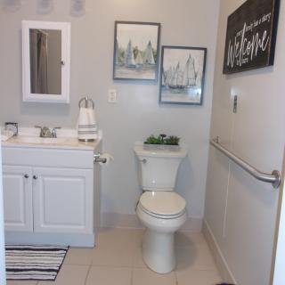 A modern bathroom with a white vanity, toilet, mirror, and decorative wall art.