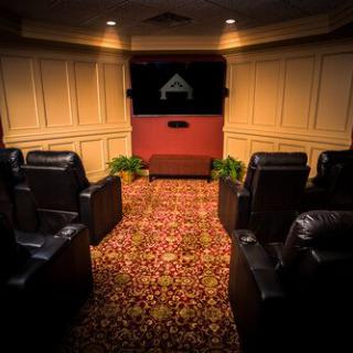 A cozy home theater with leather seating and a screen, featuring dim lighting and a patterned carpet.