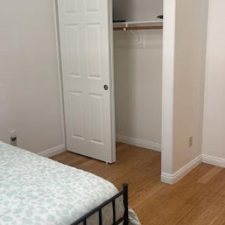 A simple and minimalist bedroom featuring a bed with light-colored bedding and an adjacent closet.