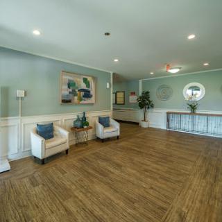 A spacious and modern lobby featuring light-colored walls, wooden flooring, and contemporary furniture.