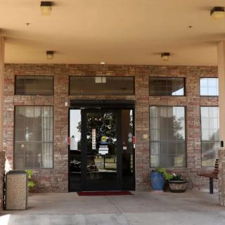 The entrance of a building with a brick facade and glass doors, adorned with potted plants.