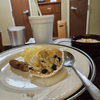 A cozy breakfast spread featuring a muffin with blueberries, sausage, and a cup of coffee.