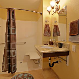 An accessible bathroom featuring a shower with a curtain and grab bars, a sink with exposed plumbing, and neatly arranged towels.