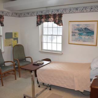 A hospital room with a patient bed, two chairs, and a window.