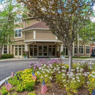 A well-maintained building entrance surrounded by landscaping with flowers and small American flags.