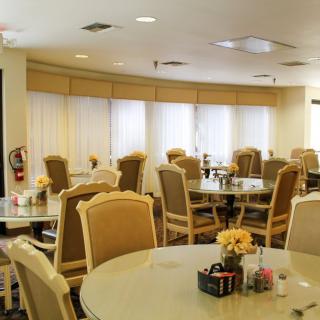 A spacious dining area with round tables and chairs, decorated with flowers and natural lighting.
