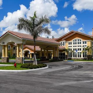 A modern residential building with palm trees and a landscaped driveway under a partly cloudy sky.
