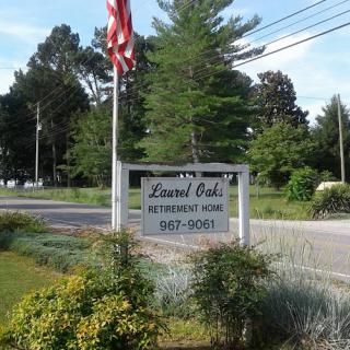 A welcoming sign for Laurel Oak restaurant, framed by greenery and an American flag.