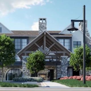 A modern building with a rustic design, featuring stone and wood elements, surrounded by trees and landscaping.