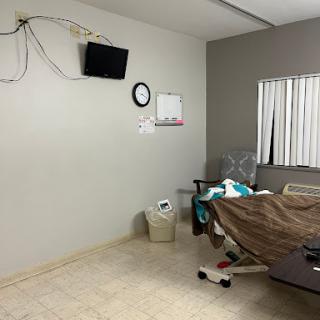 A view of a hospital room featuring a bed, a TV mounted on the wall, and a clock.