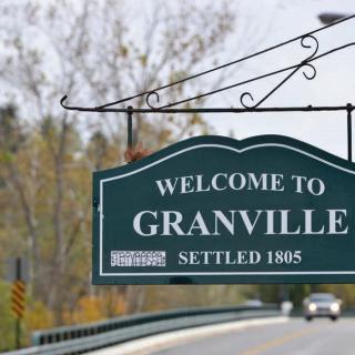 A welcome sign for the town of Granville, established in 1805, located by a road surrounded by trees.