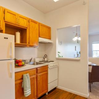 A cozy apartment kitchen with wooden cabinets, a refrigerator, stove, and sink.