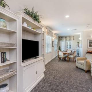 A cozy living room with a television and shelving unit, leading to a dining area.