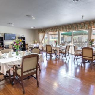 A spacious dining area with neatly arranged tables and chairs, featuring large windows and hardwood flooring.