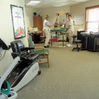 A physical therapy room with exercise equipment and therapists working with a patient.