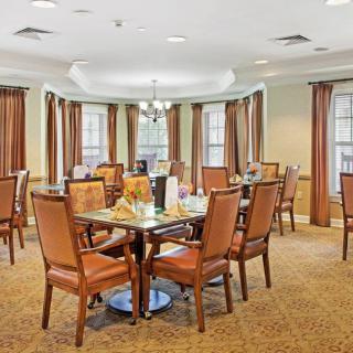 A well-furnished dining room with multiple tables and chairs, surrounded by large windows and elegant curtains.