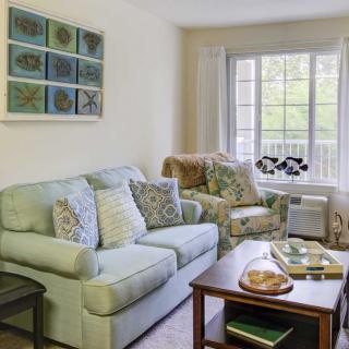 A cozy living room featuring a sofa with decorative pillows, an armchair, a coffee table, and a large window.
