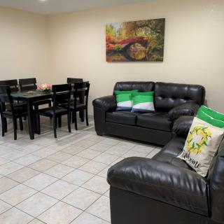 A cozy living room with black leather sofas and a dining area, featuring a colorful painting on the wall.